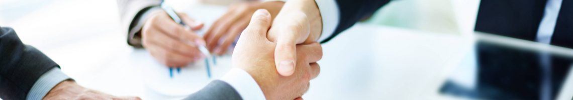 Image of business partners handshaking over business objects on workplace